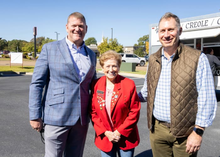Two men with a woman with her name-tag posing in a parking lot for the West Tennessee 125th anniversary