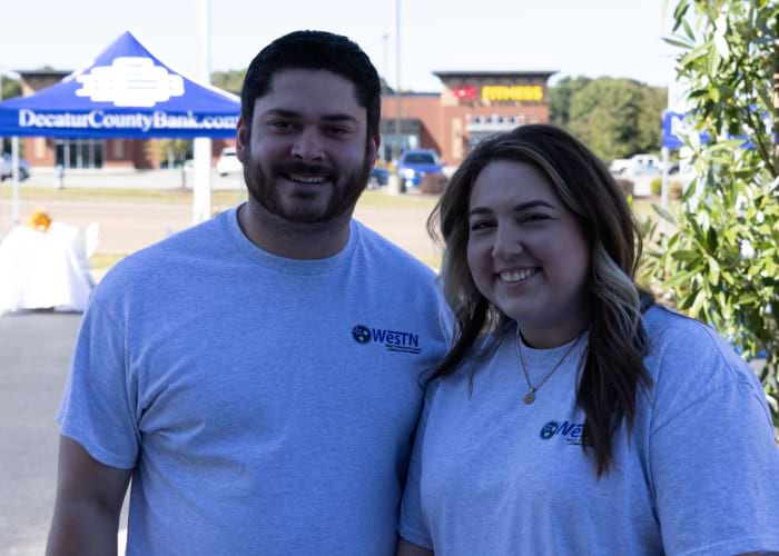 Two people with West Tennessee Bank shirts posing together in from of Decatur Bank for the West Tennessee Bank Anniversary
