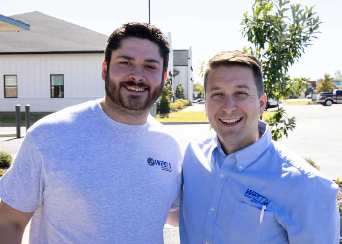 Two men with West TN Bank shirts posing for the camera for the anniversary