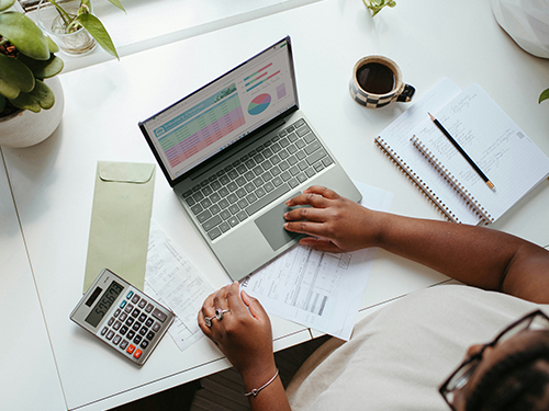 Person working at a desk with a laptop showing charts, a calculator, documents and a notebook — visualizing business valuation