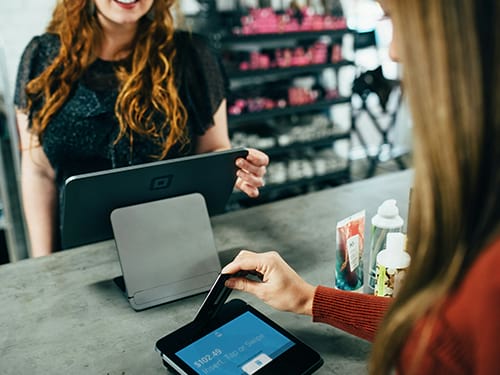 Lady standing at a checkout counter paying with her credit card