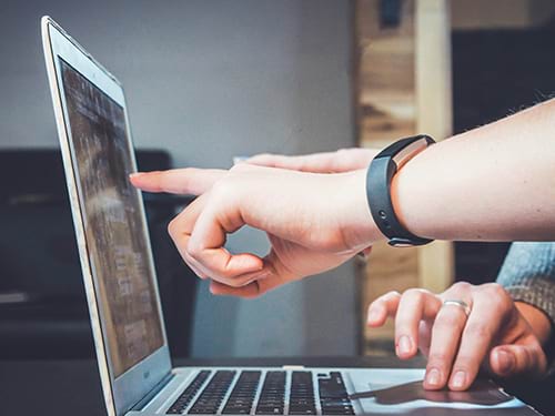 Two people sitting and looking at a computer with one person pointing at the screen