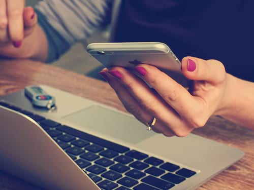 Lady with painted nails using her phone above her computer