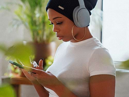 Woman on her phone with headphones on, surrounded by a clean home