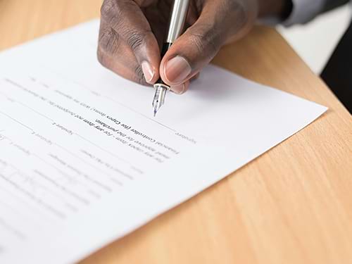 A person lowering their pen to sign their name on a financial document