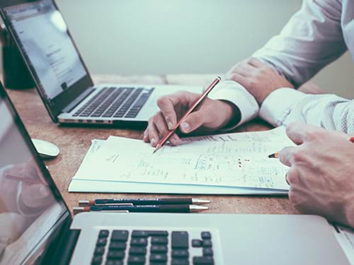 Two males working on a document together with their computers pulled up