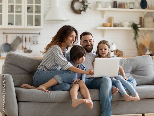A small family gathered together on a couch, looking at the computer while smiling